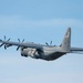 A U.S. Air Force C-130J Super Hercules military transport aircraft is captured in flight against a clear blue sky. The aircraft bears tail number 71354 and AETC (Air Education and Training Command) markings, along with a U.S. flag on the vertical stabilizer. The aircraft is painted in standard military gray and features four turboprop engines with six-bladed propellers.