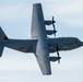 A U.S. Air Force C-130 Hercules military transport aircraft is photographed from below against a partly cloudy sky. The aircraft bears tail number 71354 and AETC (Air Education and Training Command) markings on the vertical stabilizer. The image captures the underside of the four-engine turboprop aircraft in flight.