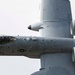 A close-up aerial photograph of a U.S. Air Force A-10 Thunderbolt II (Warthog) attack aircraft in flight, viewed from slightly above and to the side. The aircraft is painted in standard gray camouflage and displays USAF markings. A pilot is visible in the cockpit, and the aircraft's distinctive twin rear-mounted turbofan engines and GAU-8 Avenger cannon nose are clearly visible.