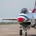 A U.S. Air Force Thunderbirds F-16 Fighting Falcon is taxiing on a runway apron, viewed from a front-facing perspective. The aircraft displays the iconic red, white, and blue Thunderbirds livery with a red nose cone. A pilot in a red helmet is visible through the bubble canopy.