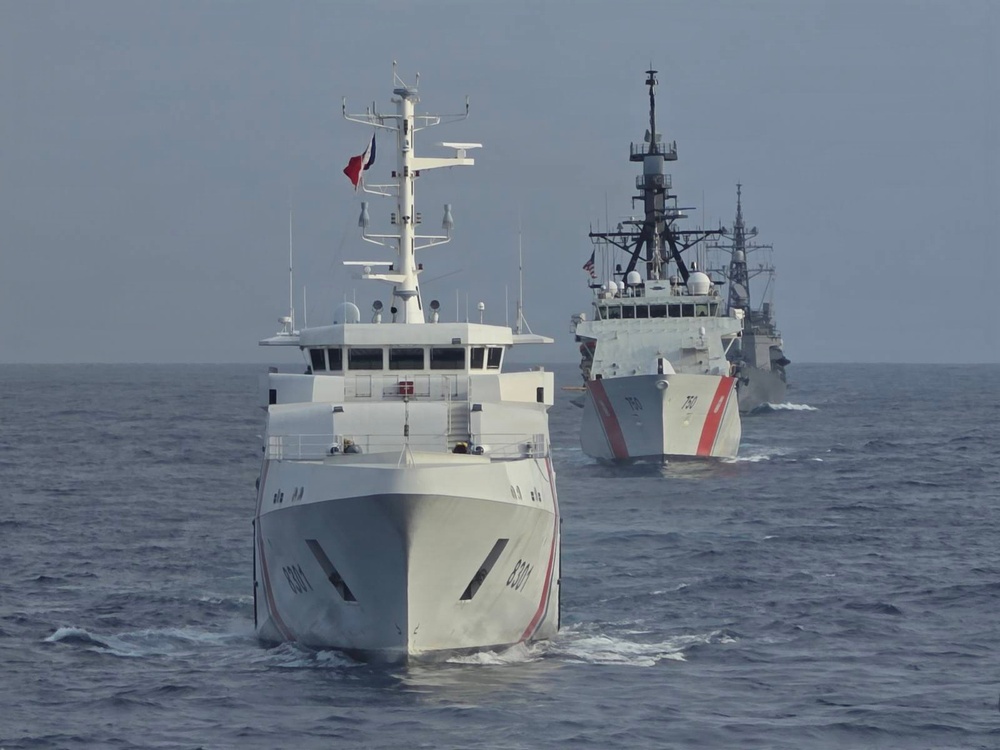 Two patrol/coast guard vessels are underway in open ocean, sailing in formation or close proximity. The foreground vessel is a white patrol boat with hull number '8301' and flies what appears to be a French tricolor flag. Behind it is a larger white vessel with red diagonal stripes and hull number '750', consistent with a US Coast Guard National Security Cutter, with a third vessel partially visible in the far background.