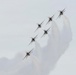 Six military jet aircraft are flying in a tight diagonal echelon formation, trailing white smoke against an overcast gray sky. The aircraft appear to be the U.S. Air Force Thunderbirds aerobatic demonstration team, identifiable by their distinctive red, white, and blue livery. The formation is climbing or banking at an angle, producing a dramatic smoke trail effect.
