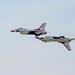 Two U.S. Air Force Thunderbirds F-16 Fighting Falcon jets are performing a close formation maneuver during an airshow. The lower aircraft is flying inverted (upside down) while the upper aircraft flies in normal orientation, demonstrating a signature Thunderbirds pass. Both aircraft display the distinctive red, white, and blue Thunderbirds livery.